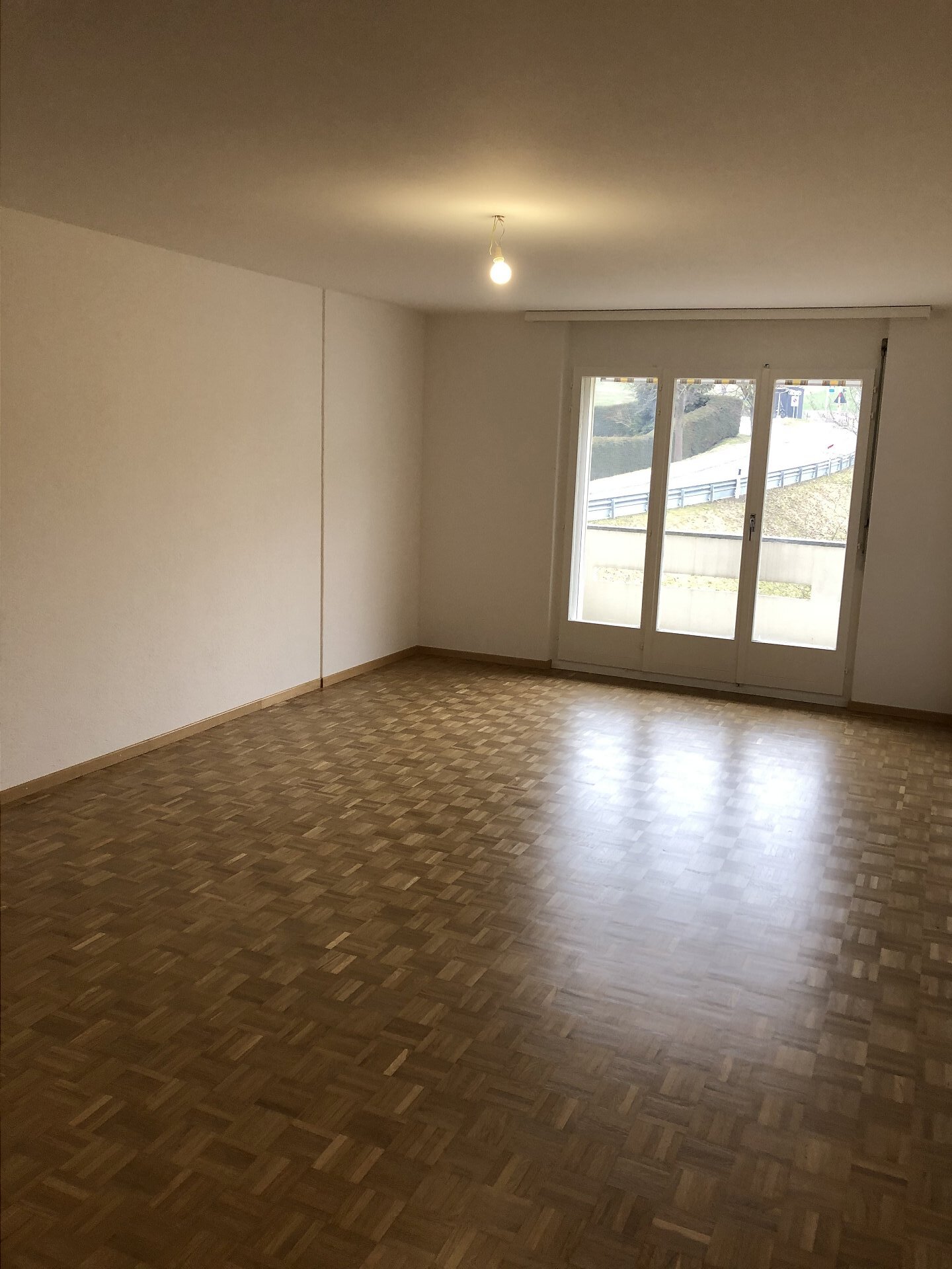 Leerer Wohnraum mit Parkett und Balkontür