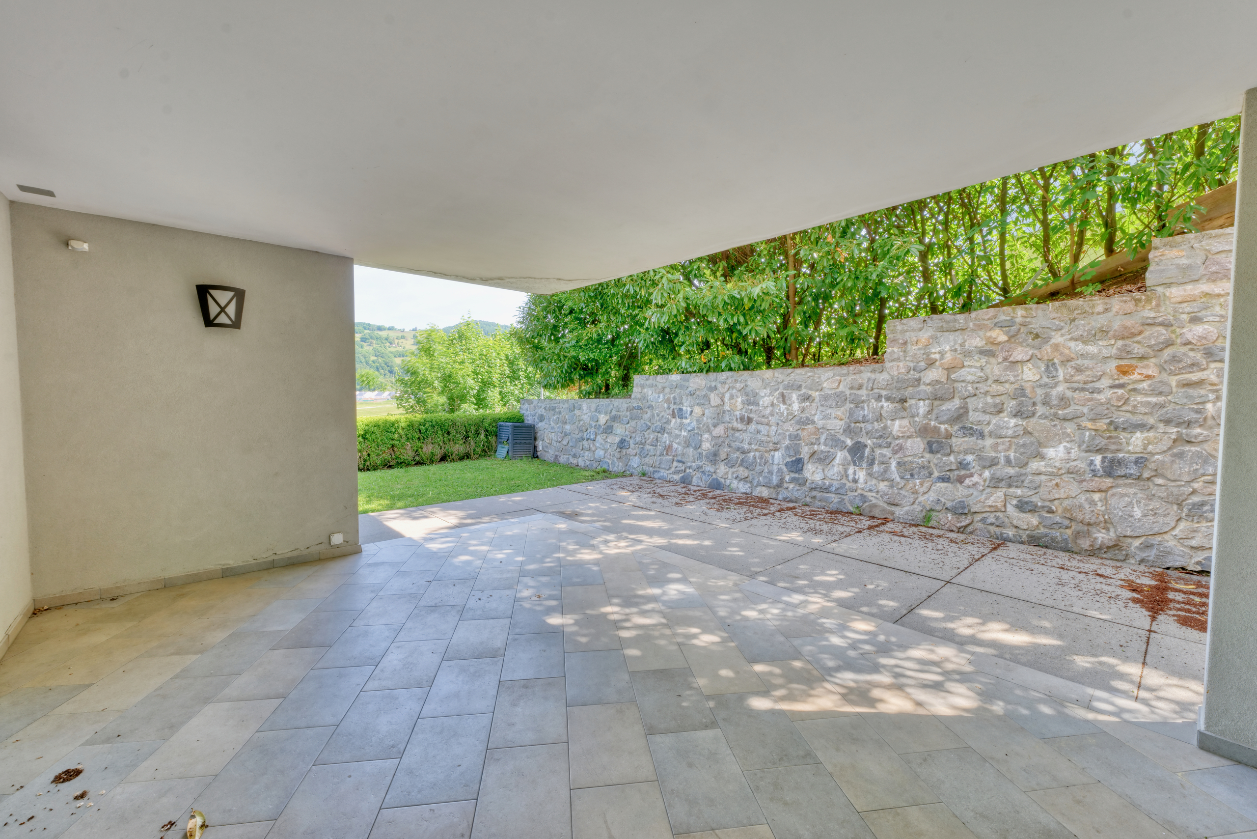 Überdachte Terrasse mit Natursteinmauer und Gartenblick