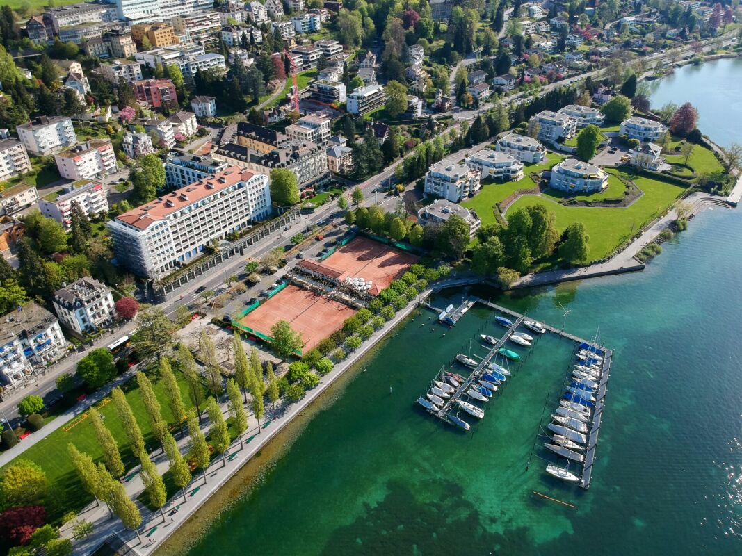 Luftaufnahme einer Uferlage mit Hafen, Tennisplätzen und Wohnbebauung