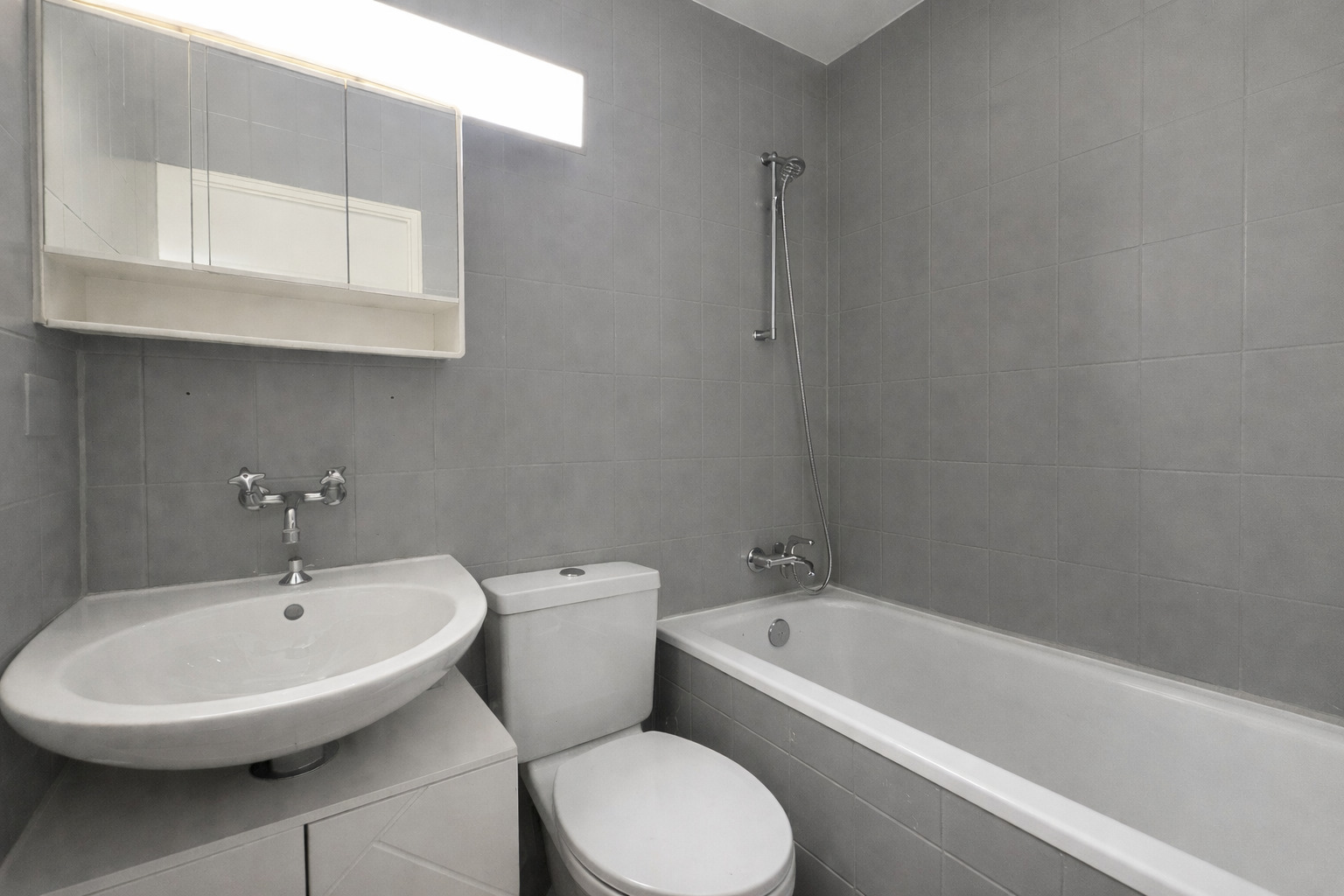 Kleines graues Badezimmer mit Badewanne, WC und Waschtisch