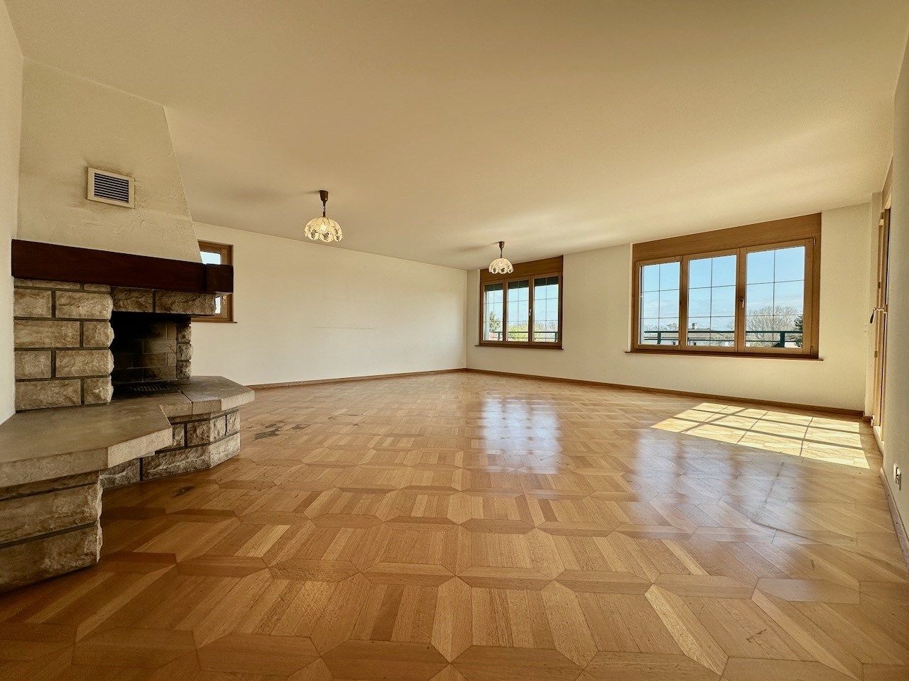 Großer leerer Wohnraum mit Kamin und Holzfenstern
