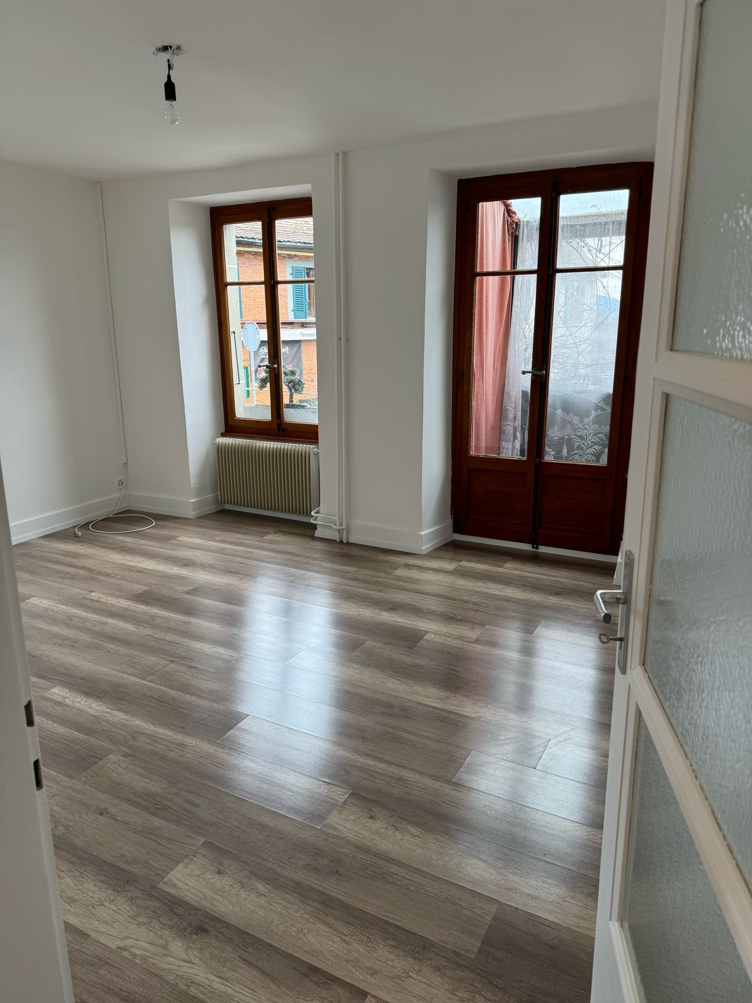 Helles, leeres Zimmer mit Holzboden und zwei Fenstern