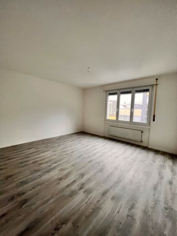 Leerer heller Wohnraum mit Fenster und Laminatboden