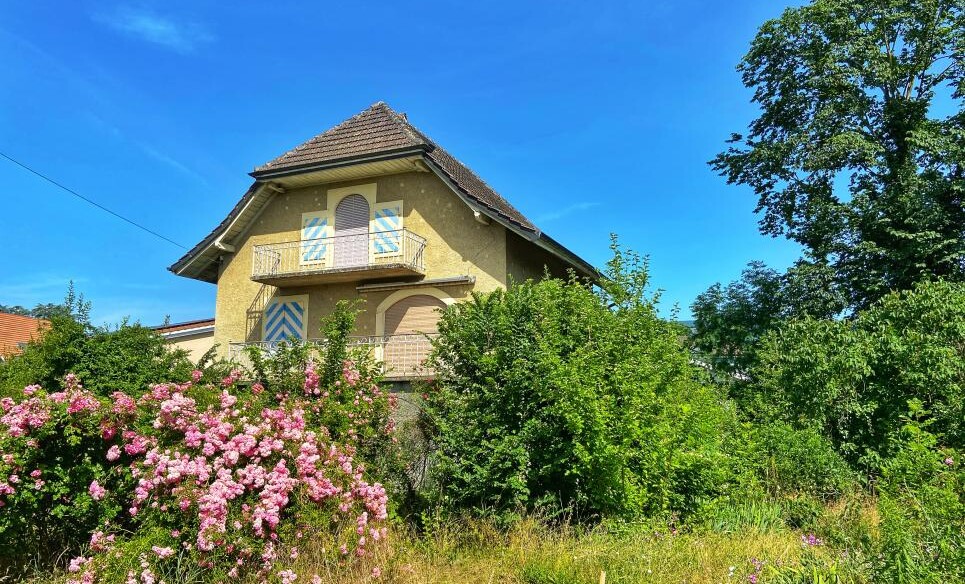 Zweigeschossiges Haus mit Balkon in grüner Gartenumgebung