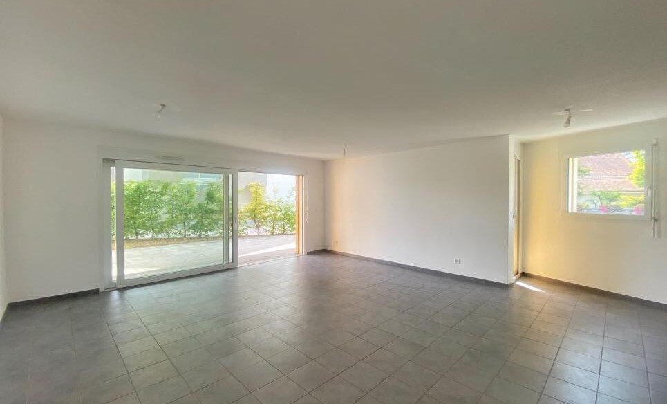 Großer leerer Wohnraum mit Terrassentür und Fenster