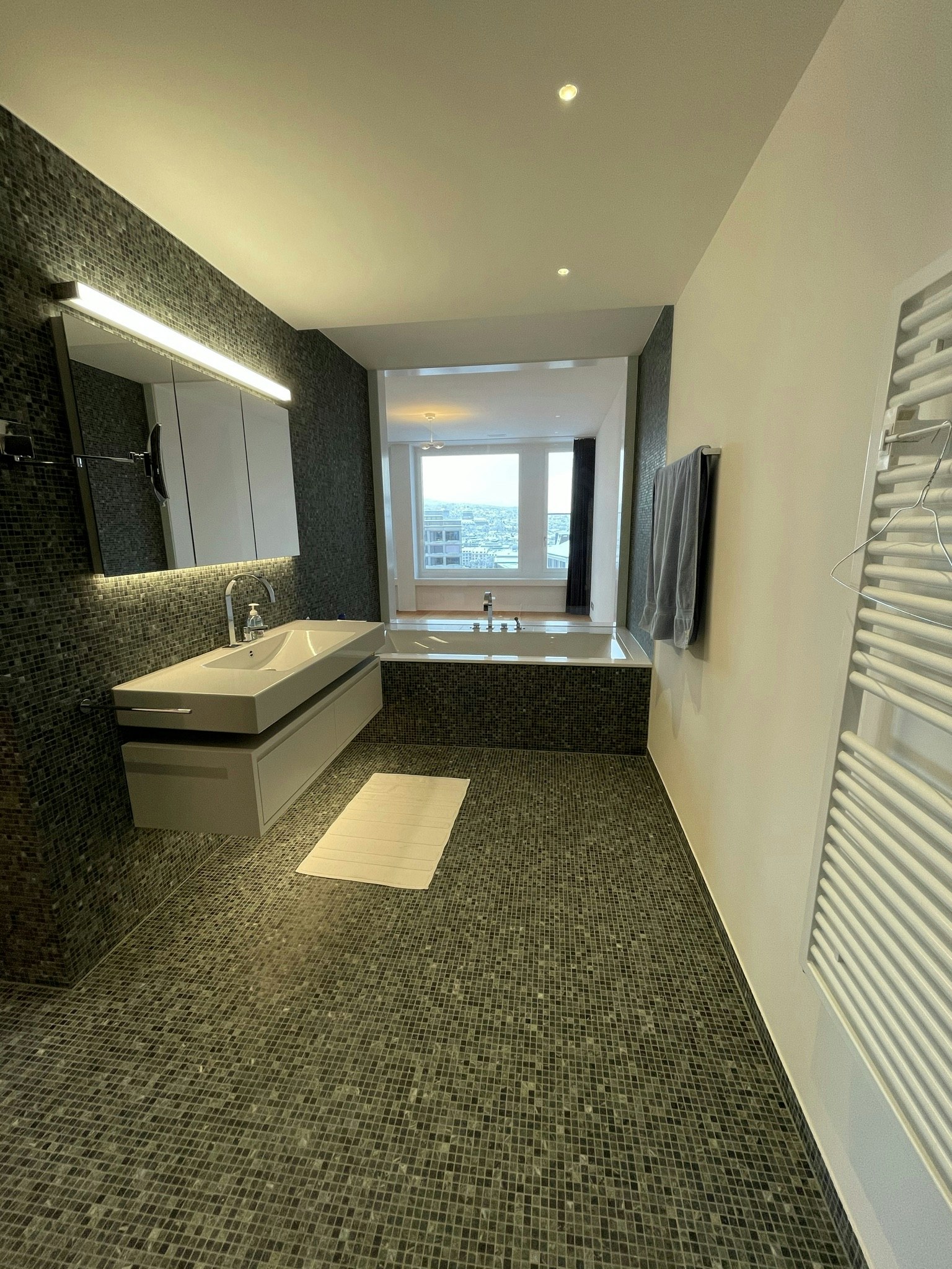 Modernes Badezimmer mit dunkler Mosaikverkleidung und Badewanne