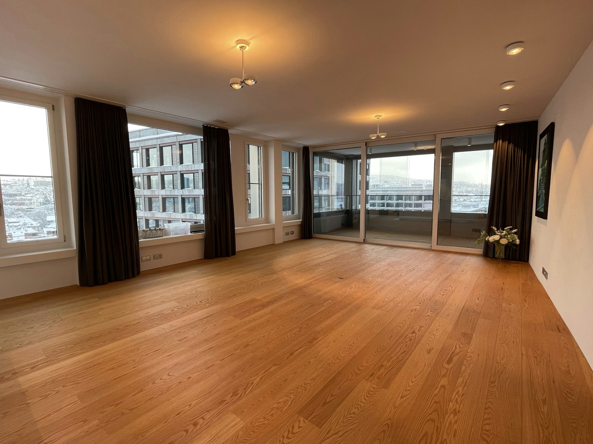 Großer leerer Wohnraum mit Panoramafenstern und Balkonzugang