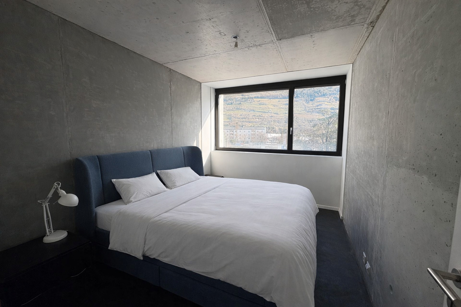 Modernes Schlafzimmer mit Betonwänden und Bergblick