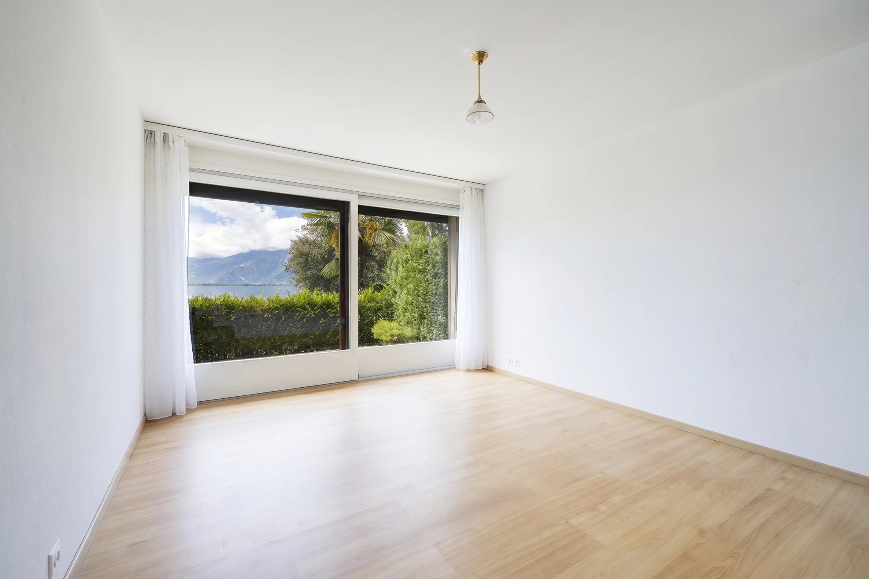Leerer, heller Raum mit Balkon- bzw. Terrassentür und Seeblick