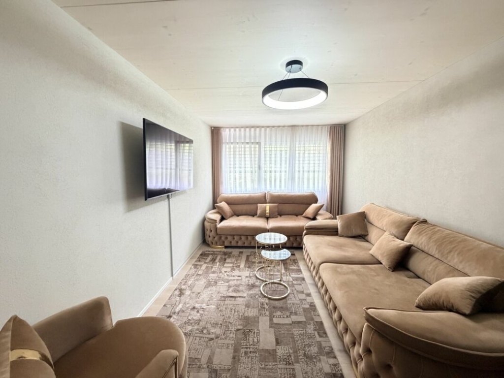 Langer, schmaler Wohnraum mit drei Sofas und Wand-TV