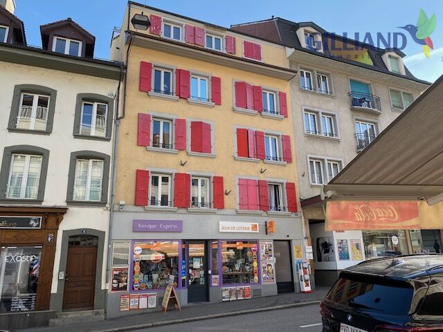 Straßenansicht eines mehrstöckigen Wohn- und Geschäftshauses mit roten Fensterläden