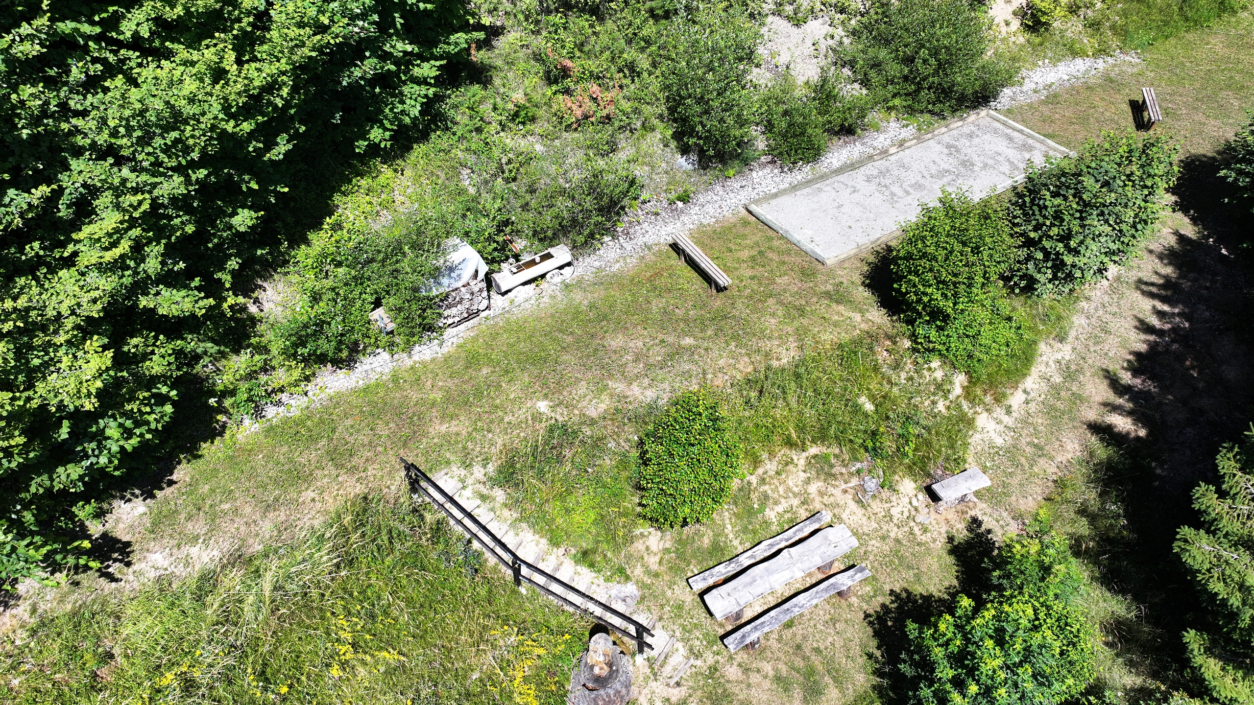 Blick auf eine naturnahe Außenfläche mit Sitzbereich und befestigter Fläche