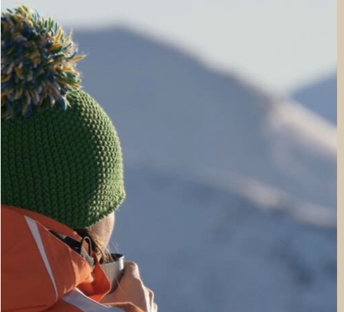 Winterliche Person mit Mütze vor Bergkulisse