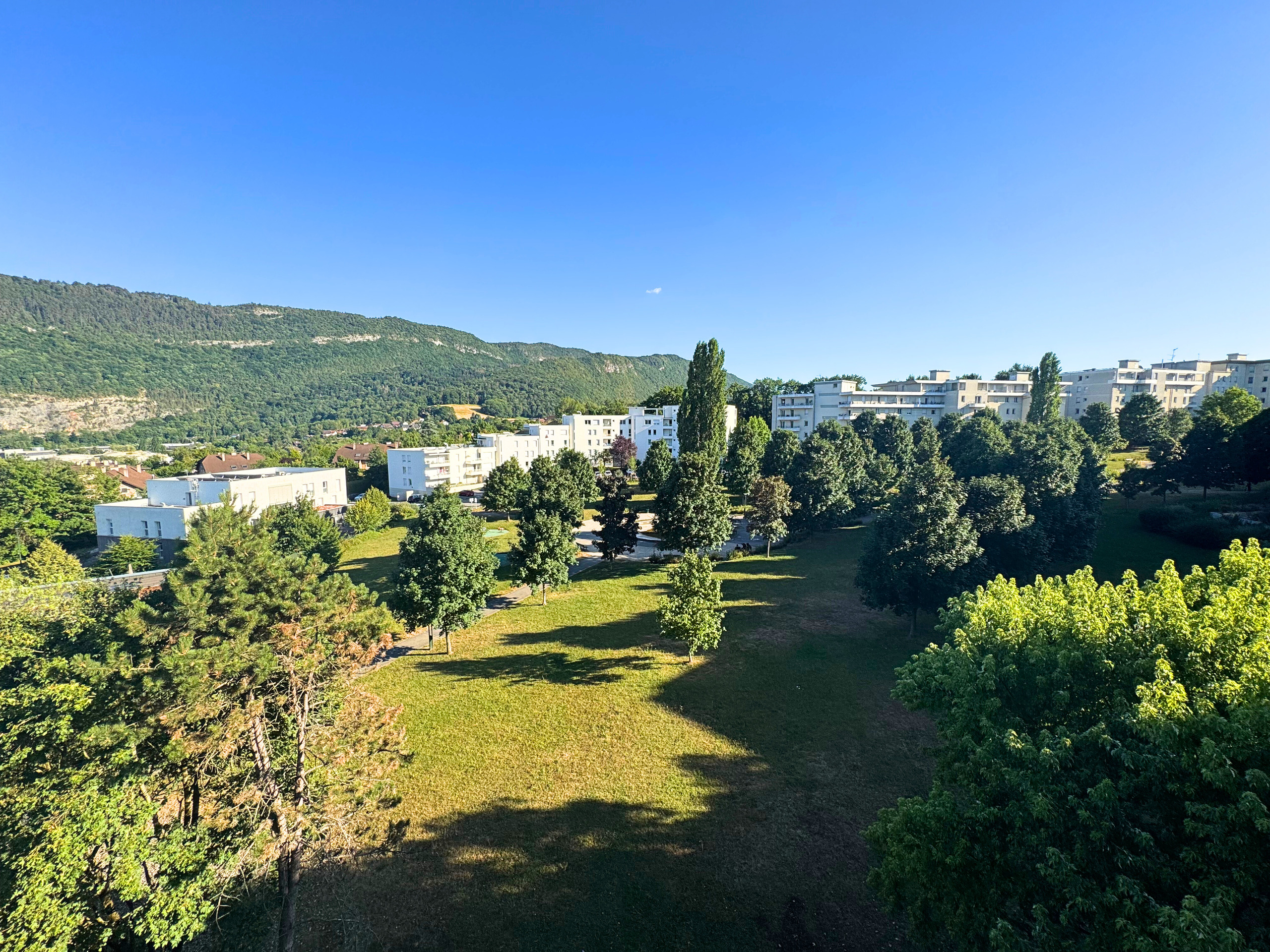 Blick über Grünflächen und Wohngebäude mit Bergkulisse