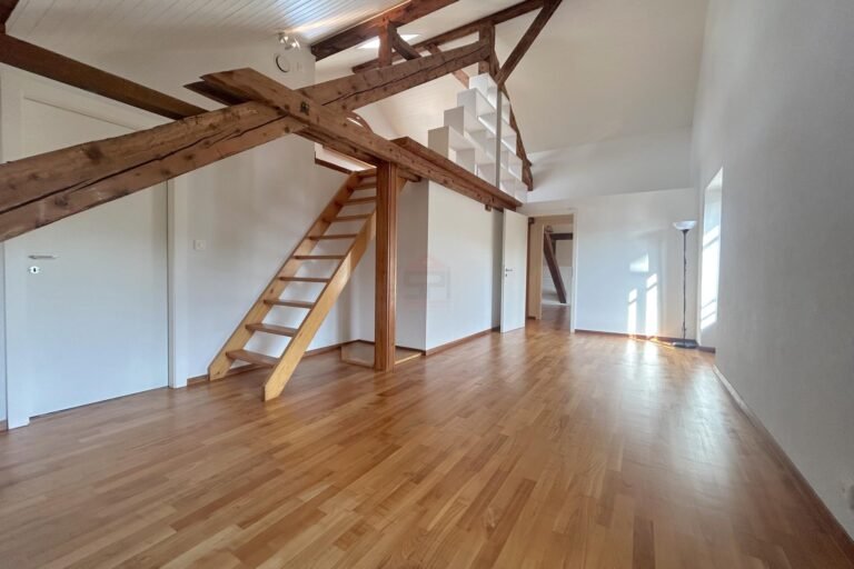 Großer leerer Wohnraum mit sichtbaren Holzbalken und Galerie