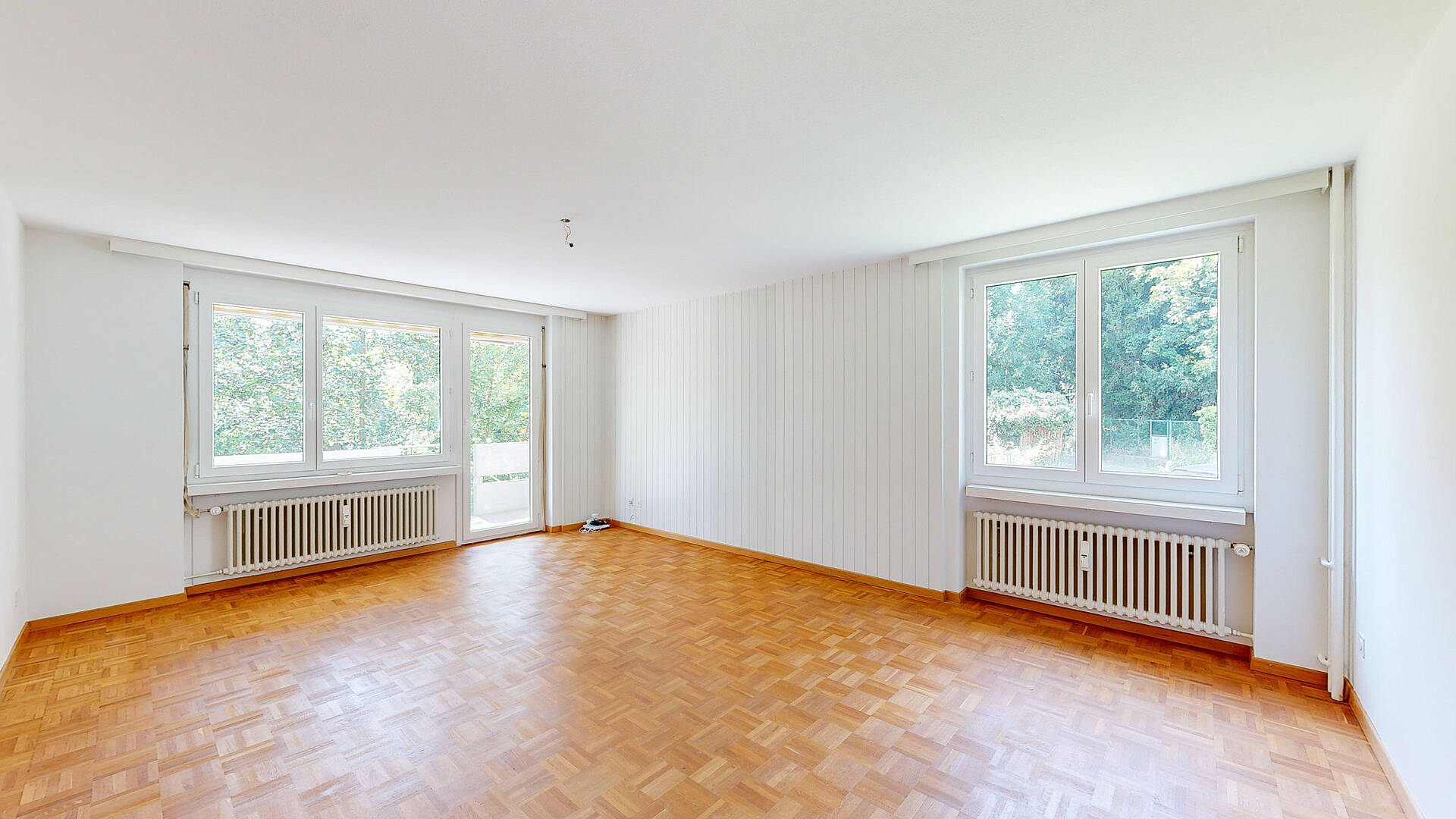 Heller leerer Wohnraum mit Parkett und großen Fenstern
