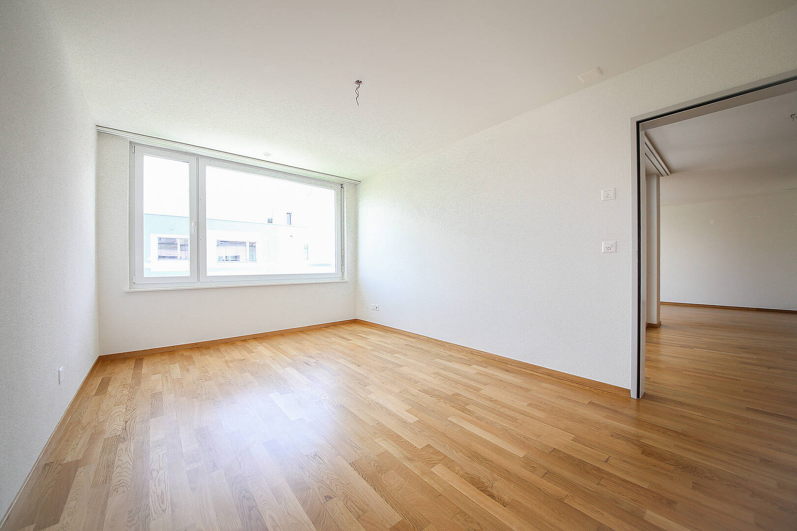 Heller, leerer Wohnraum mit Parkett und großem Fenster