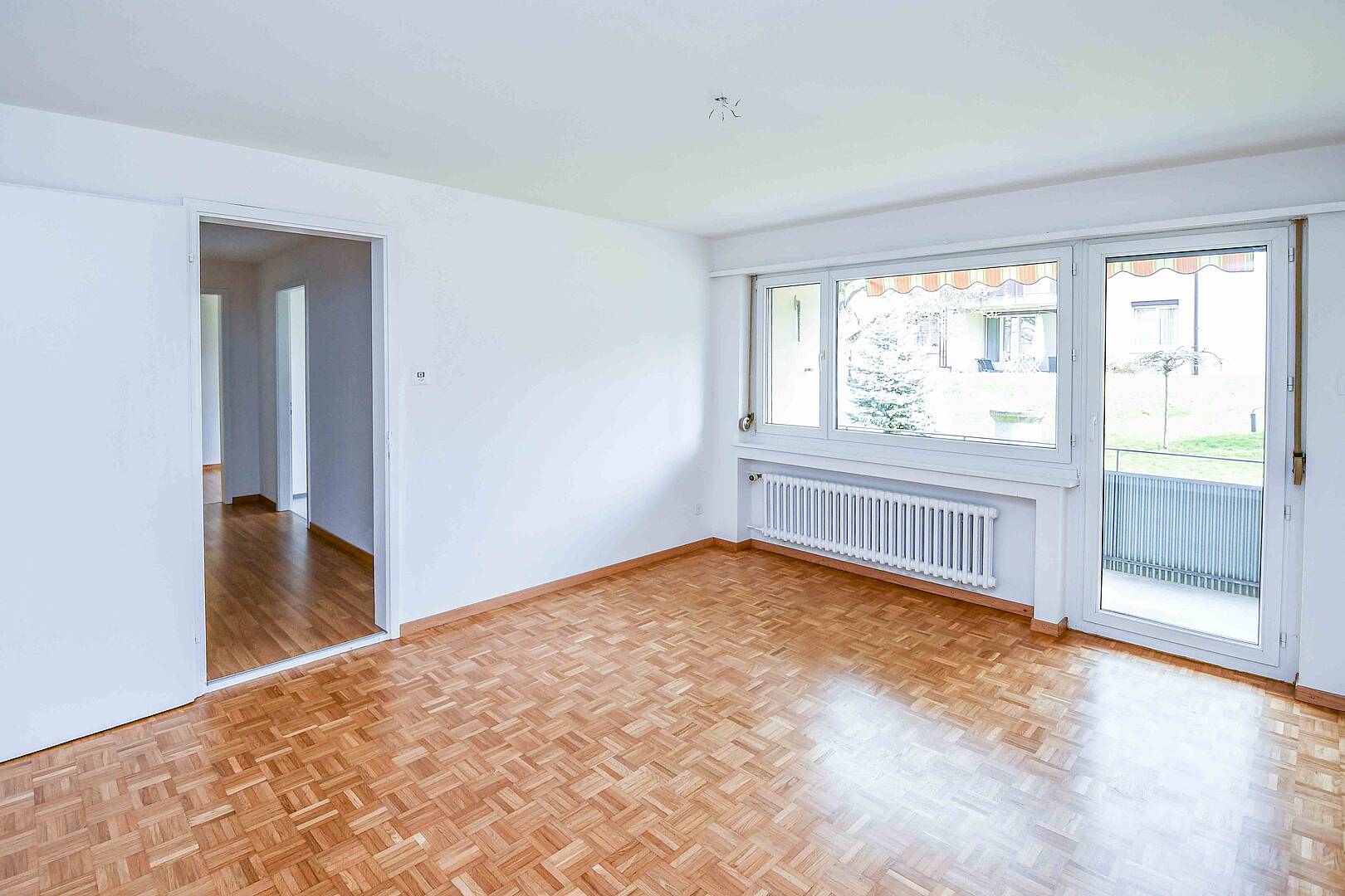 Heller leerer Wohnraum mit Parkett und Balkonzugang