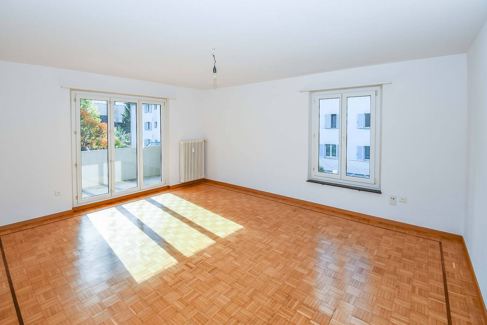 Leerer Wohnraum mit Balkon und zwei Fenstern