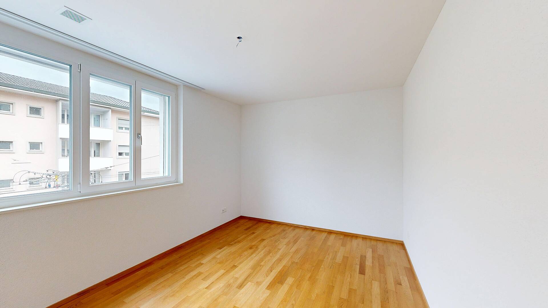 Heller leerer Raum mit Parkettboden und großem Fenster