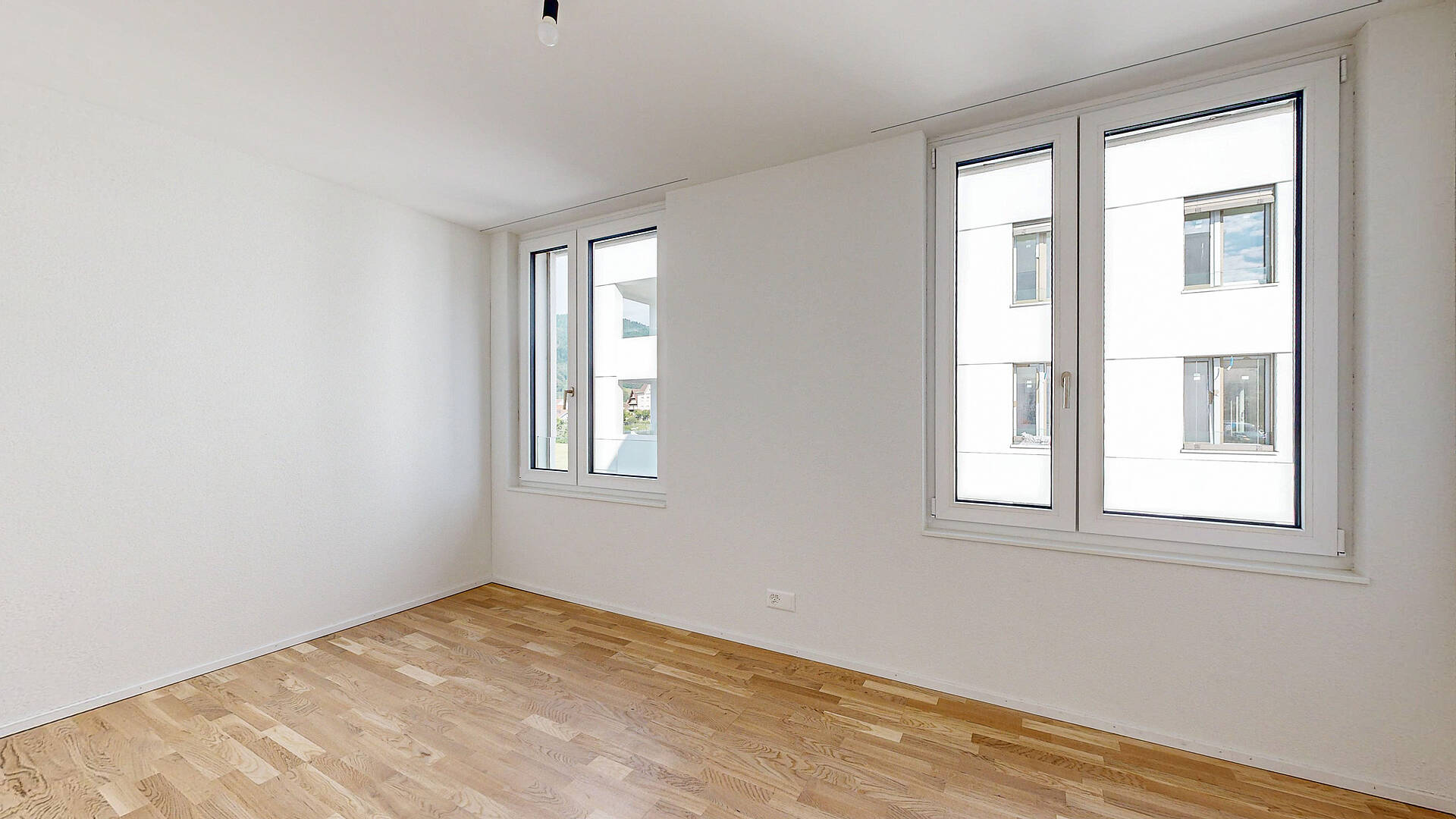 Helles leeres Zimmer mit Holzfußboden und großen Fenstern