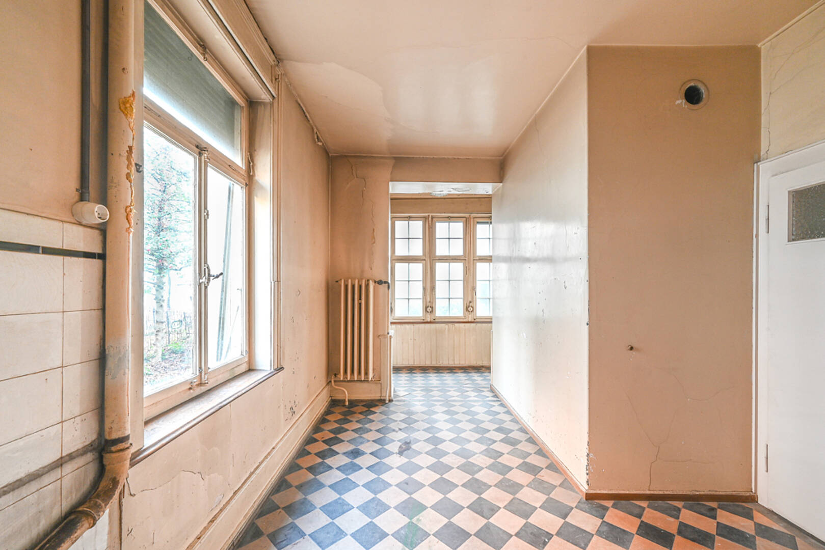 Renovierungsbedürftiger Flur mit Kassettenfenstern und Fliesenboden