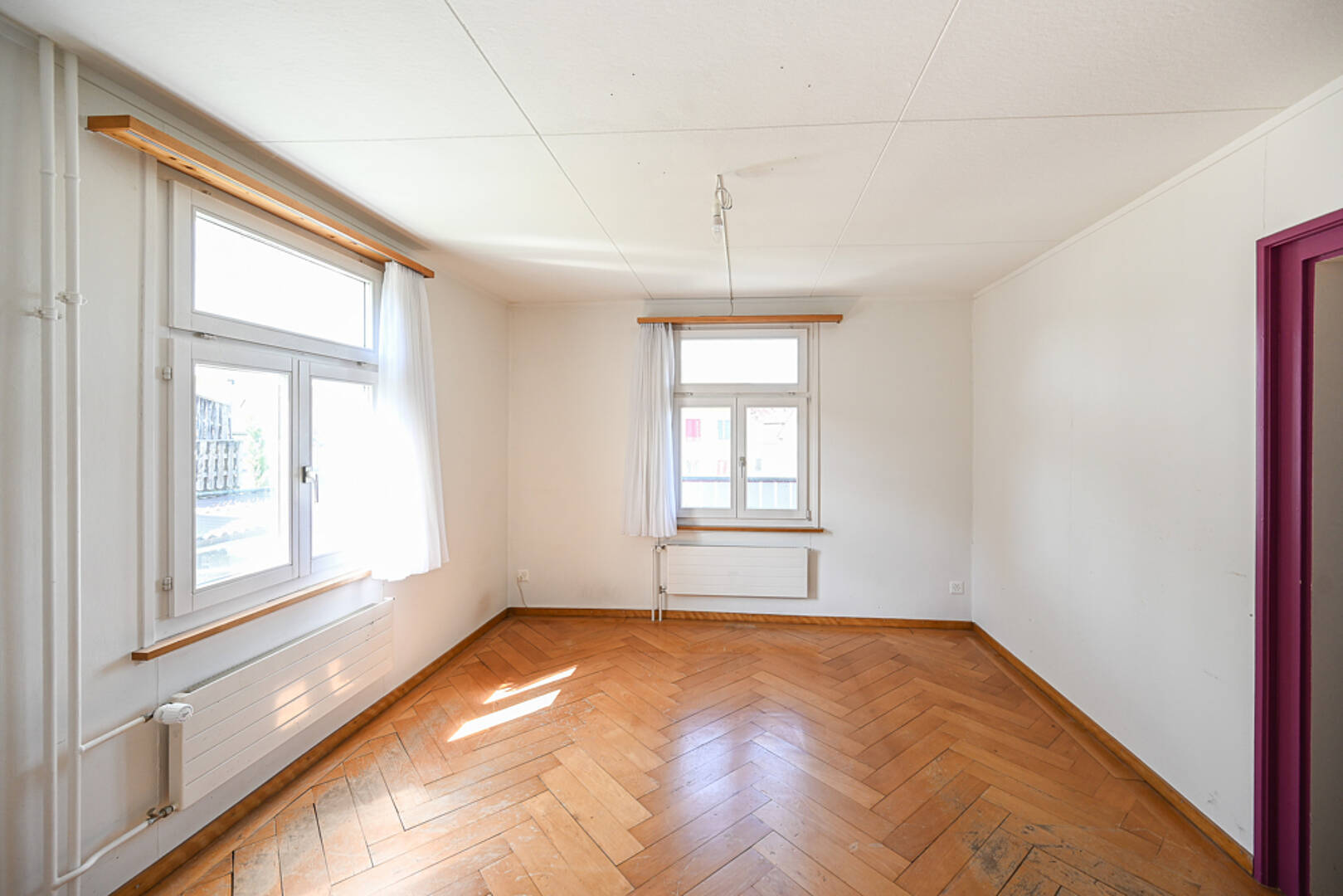 Heller leerer Raum mit Parkettboden und zwei Fenstern