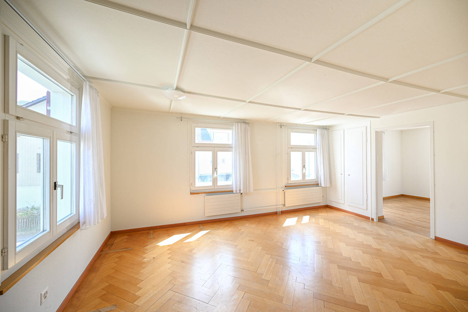 Heller leerer Wohnraum mit Parkett und vielen Fenstern