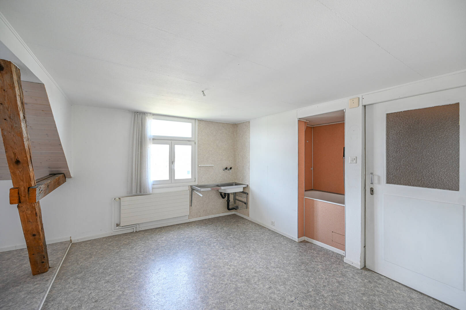 Heller, leerer Innenraum mit Fenster, Spüle und sichtbarem Holzbalken