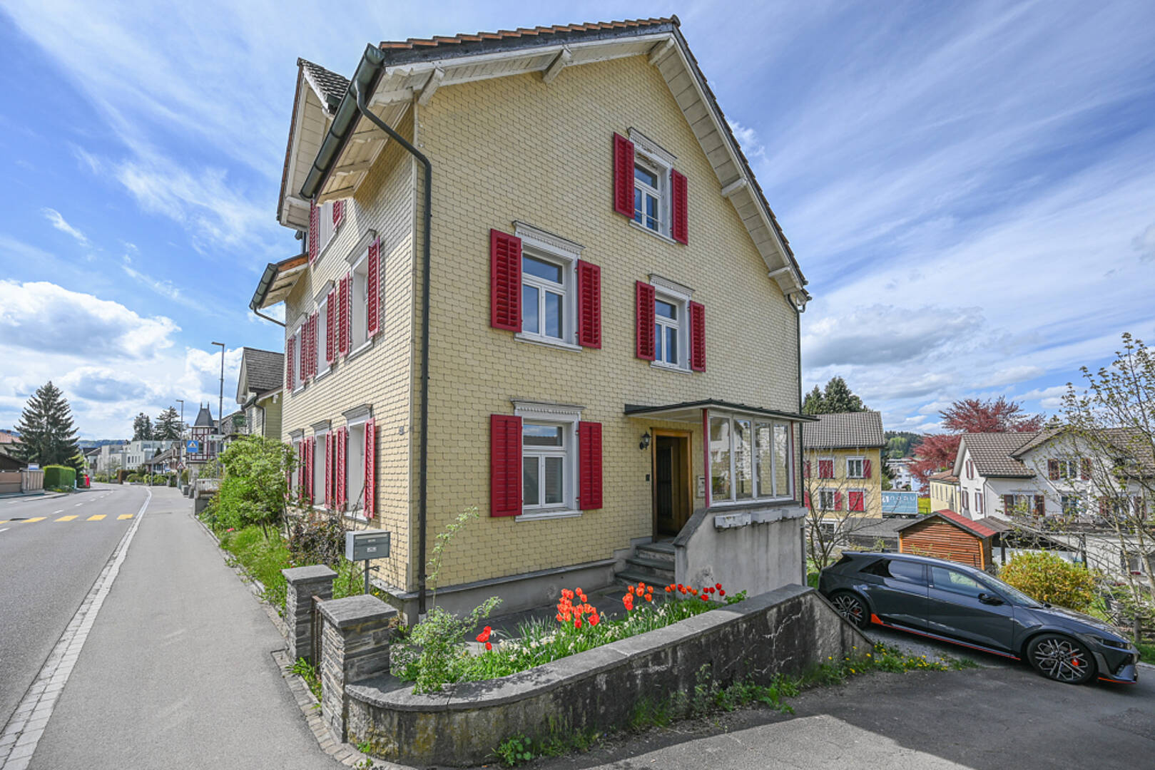 Freistehendes Wohnhaus mit roter Fensterläden und Straßenansicht