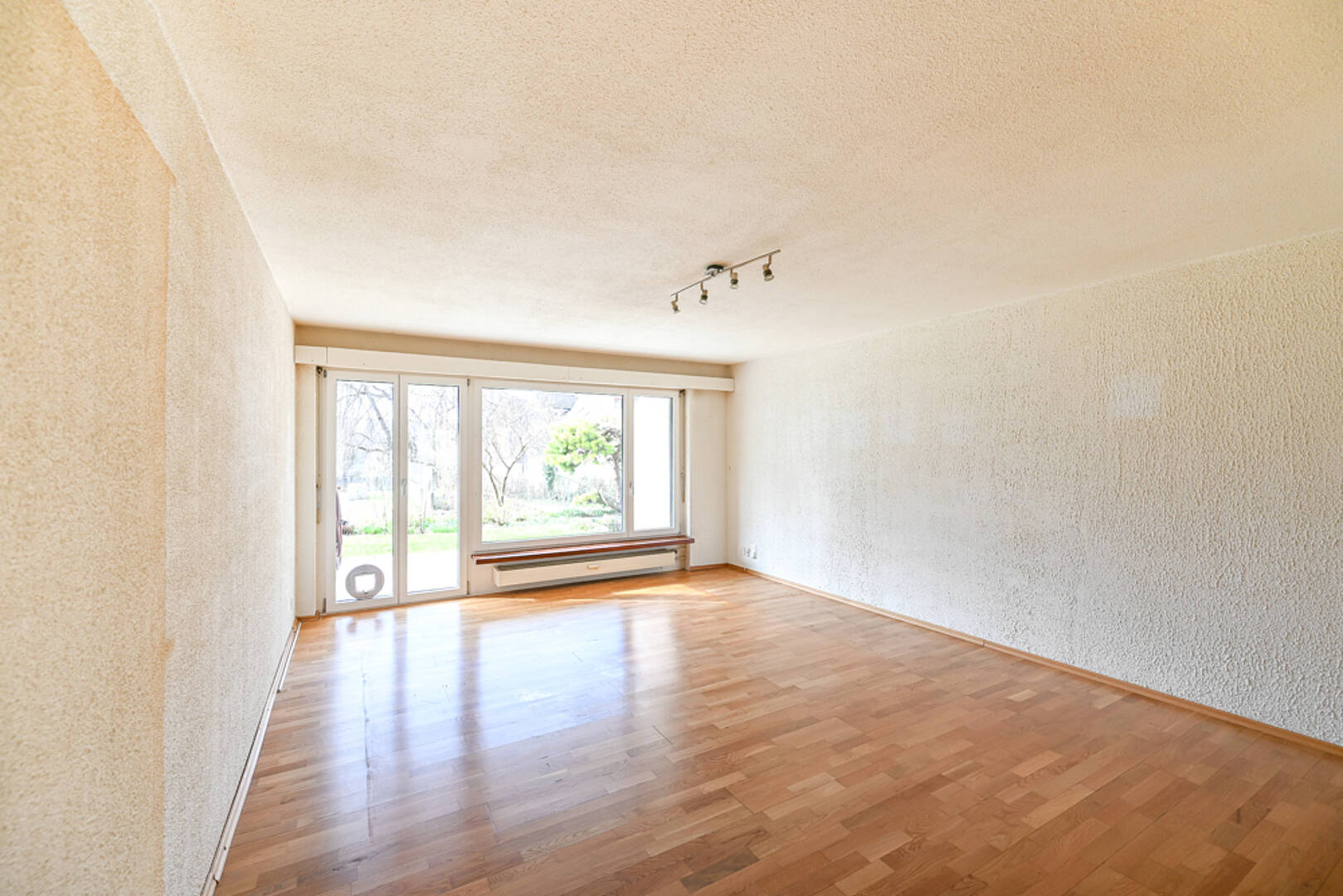 Heller leerer Wohnraum mit Parkett und großem Fenster