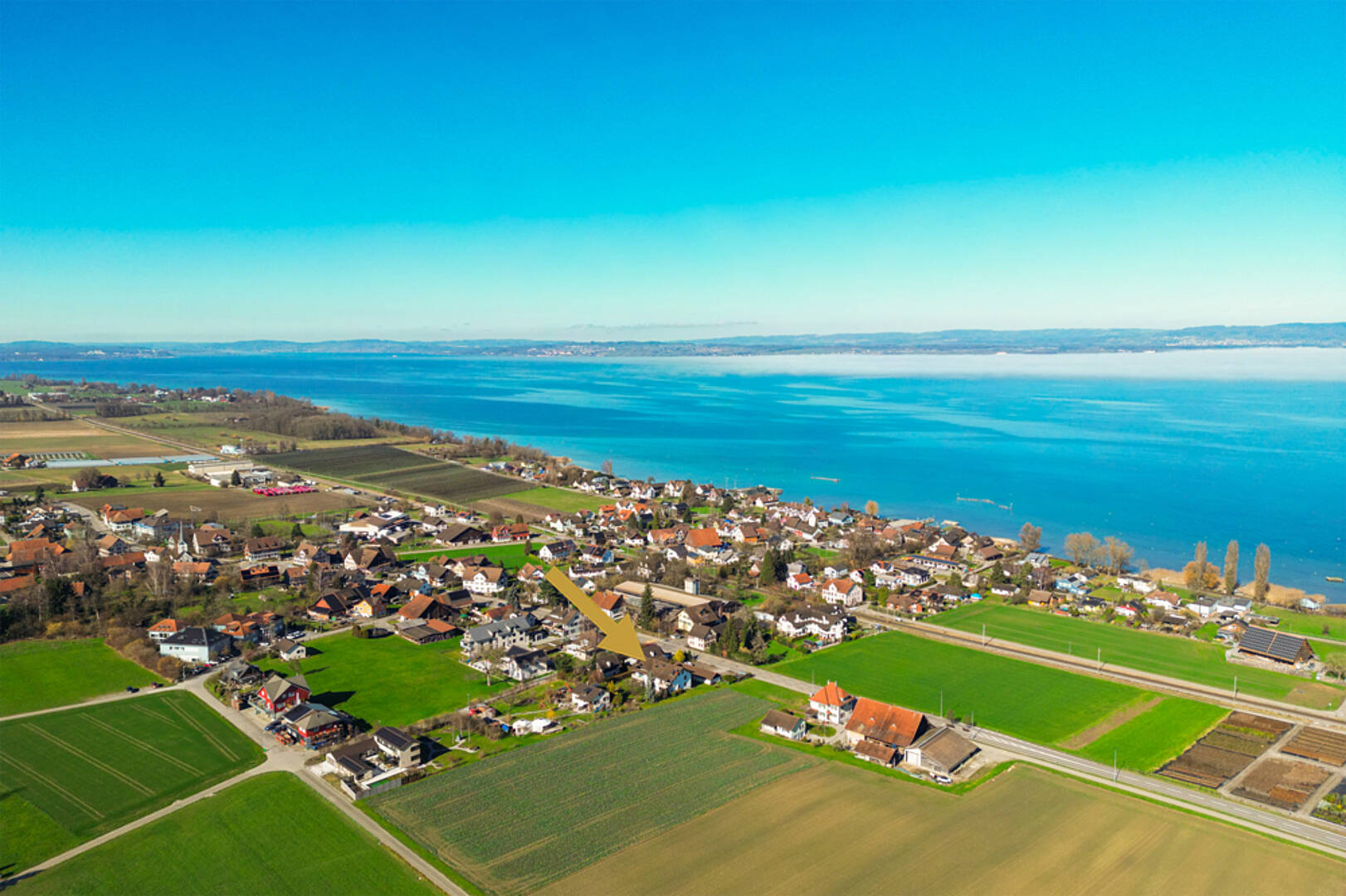 Luftaufnahme eines Seeufers mit Siedlung und Feldern