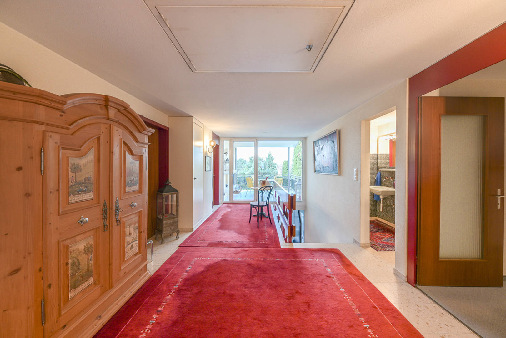 Heller Flur mit rotem Teppich und Holzschrank