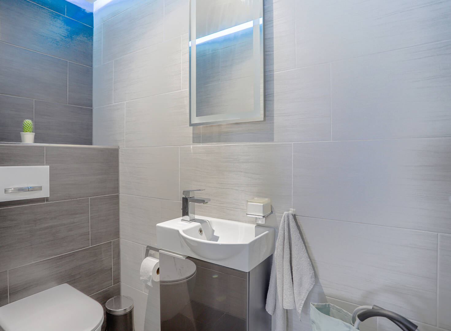 Modernes Gäste-WC mit grauen Fliesen und Wandwaschbecken