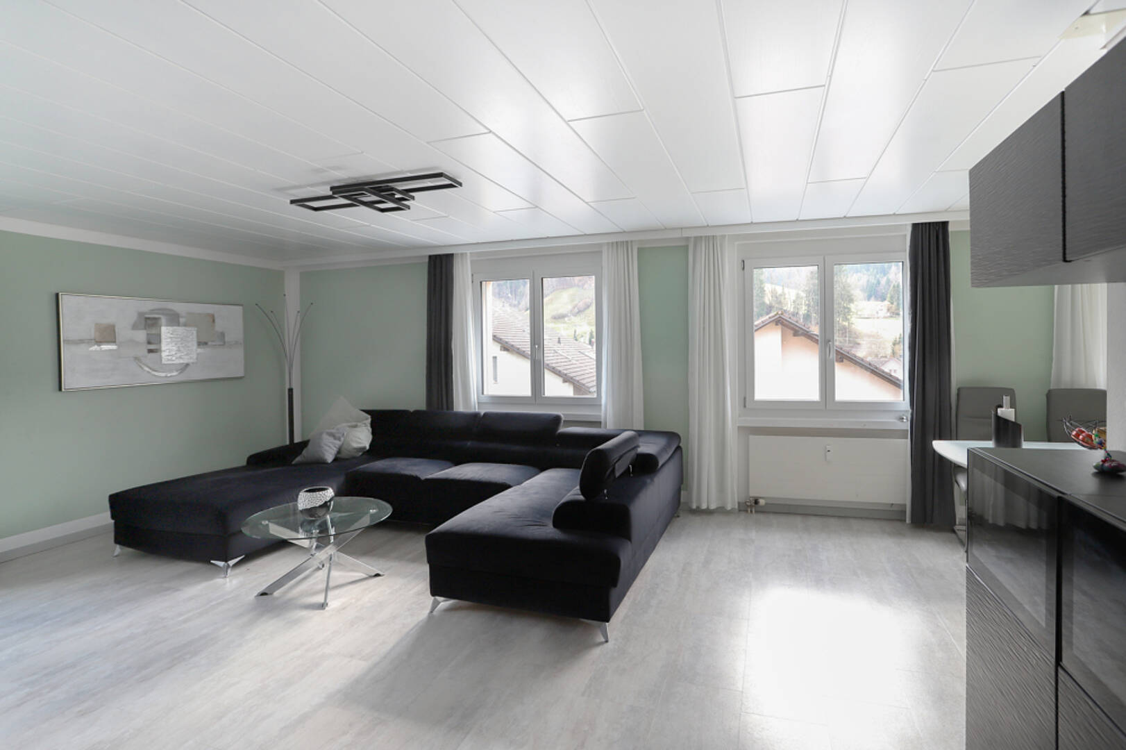 Modernes Wohnzimmer mit Ecksofa und großen Fenstern