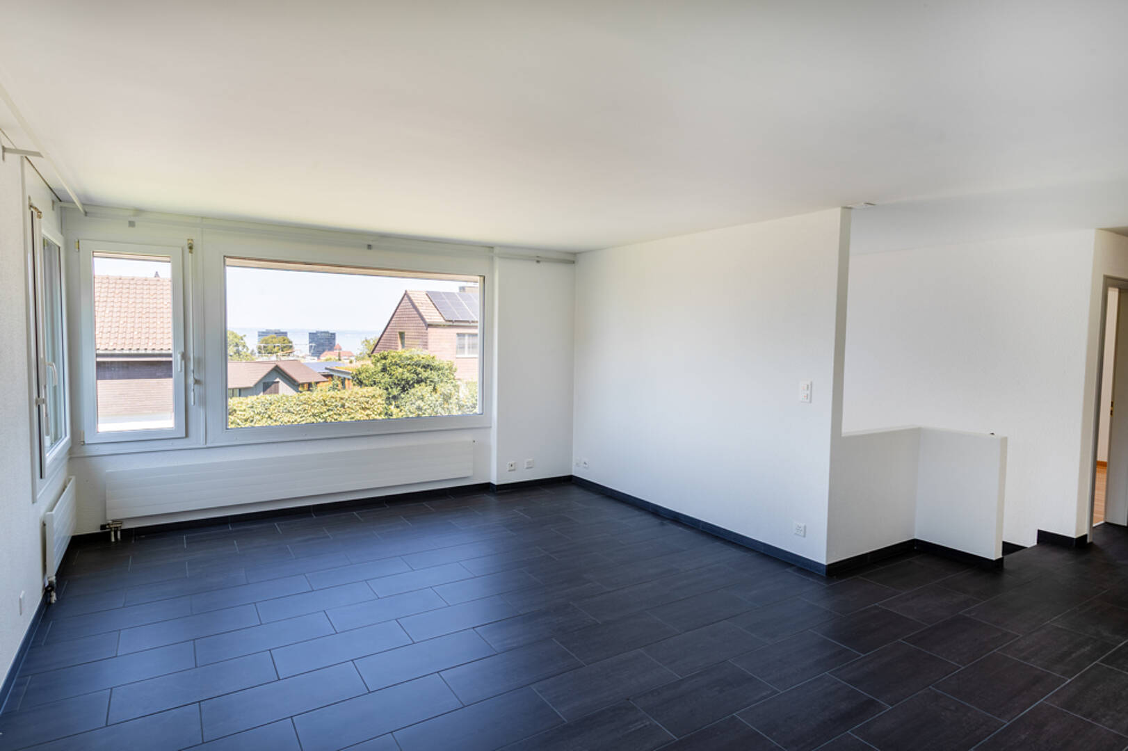 Heller leerer Wohnraum mit großem Fenster und dunklem Boden