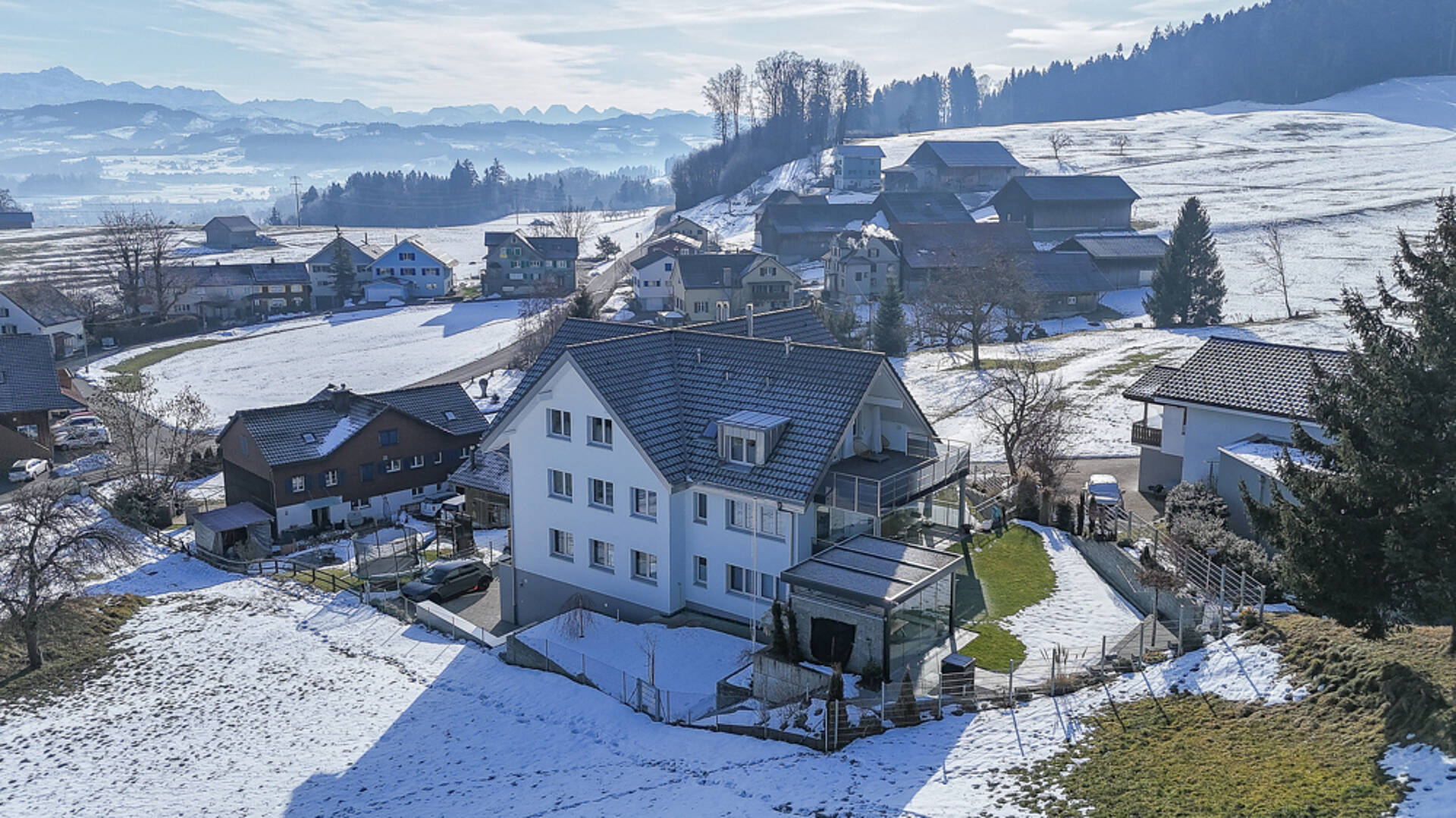 Schneebedeckte Wohnhäuser in alpiner Hügellandschaft