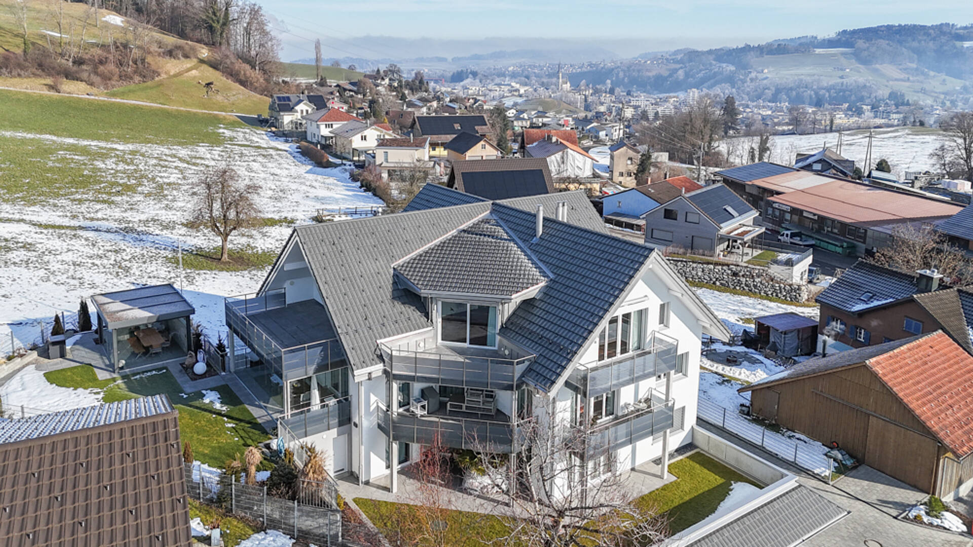 Luftaufnahme eines modernen Einfamilienhauses in winterlicher Hanglage