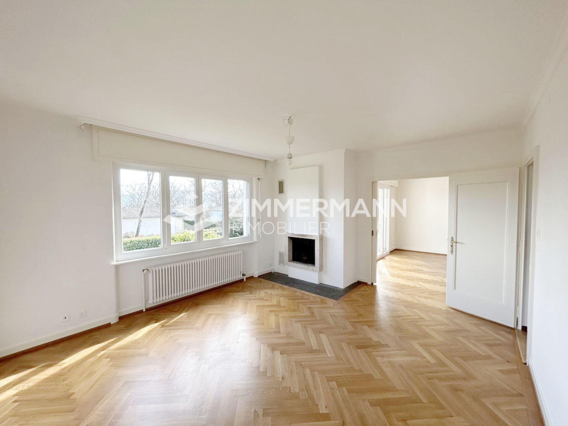 Heller leerer Wohnraum mit Parkett, Fenster und Kamin