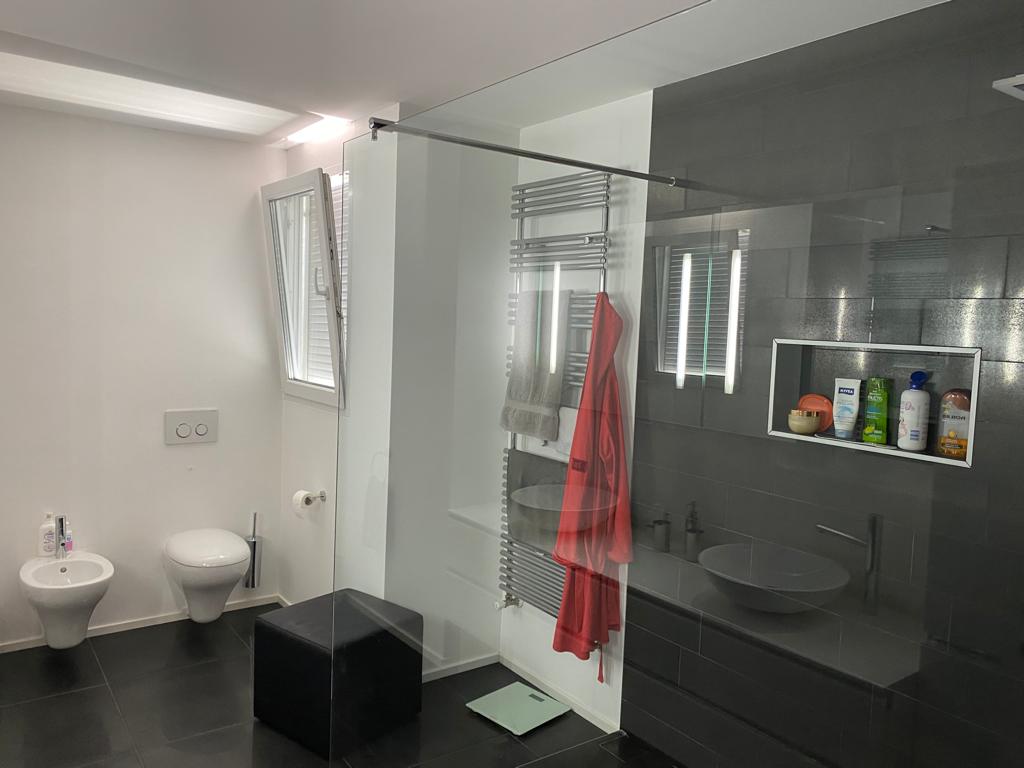 Modernes Badezimmer mit dunklen Fliesen und Glasabtrennung