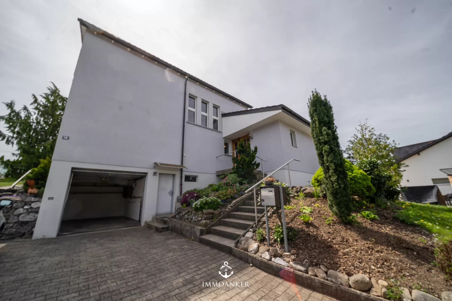 Außenansicht eines modernen Einfamilienhauses mit Garage und Gartenhang