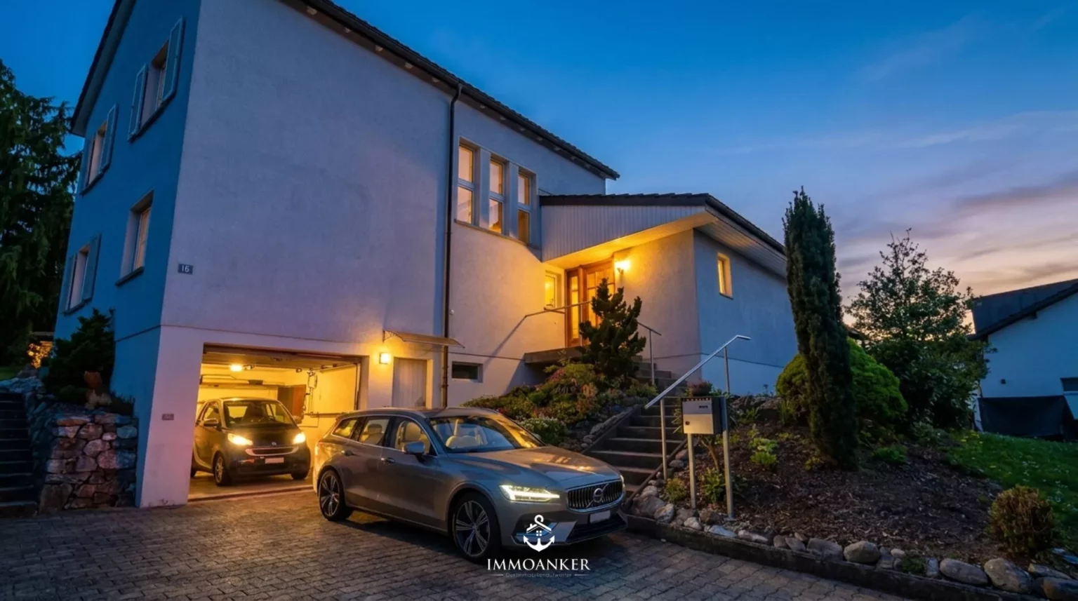 Abendliche Außenansicht eines Einfamilienhauses mit Garage und Zufahrt