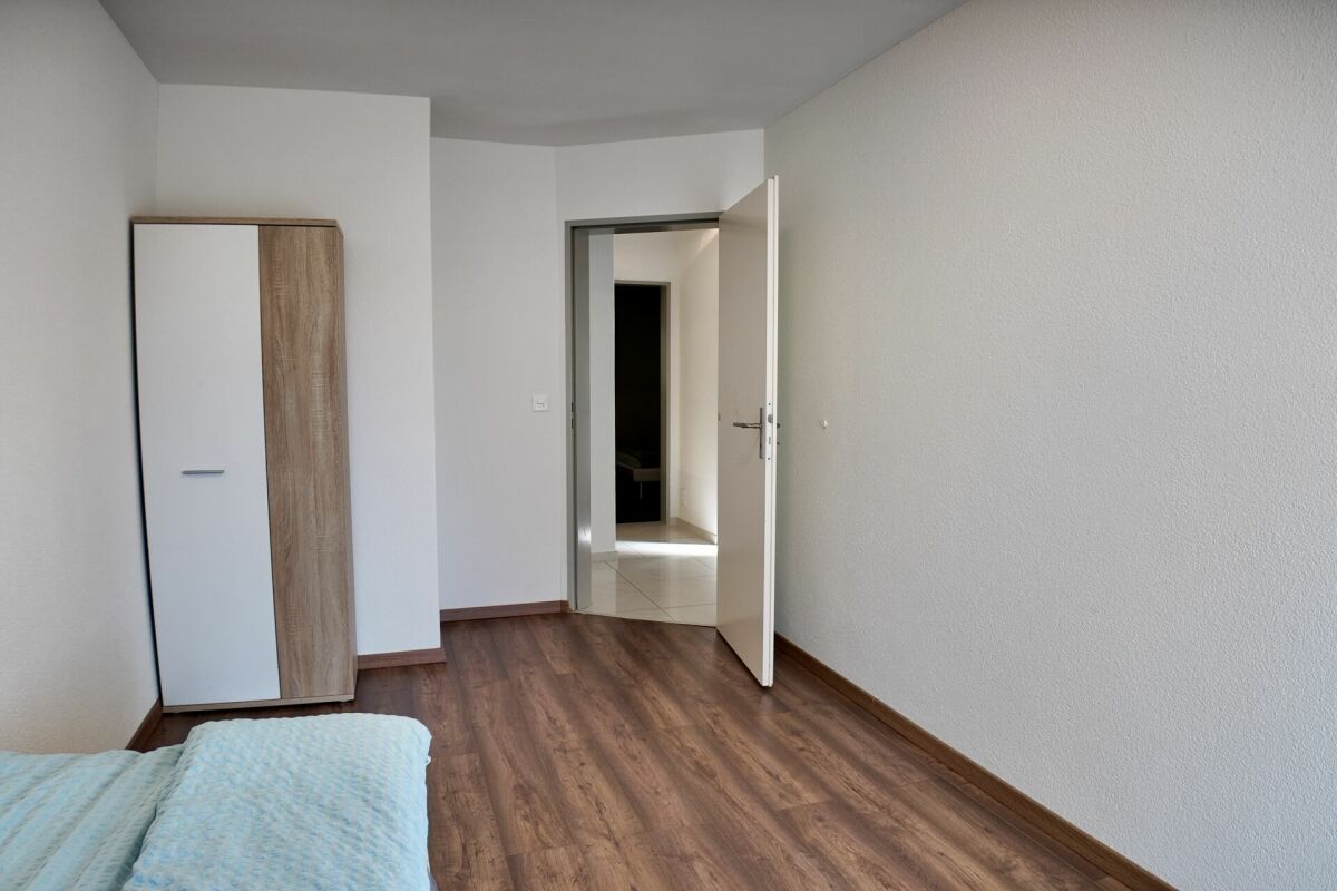 Helles Schlafzimmer mit Holzoptik-Boden und offenem Türblick