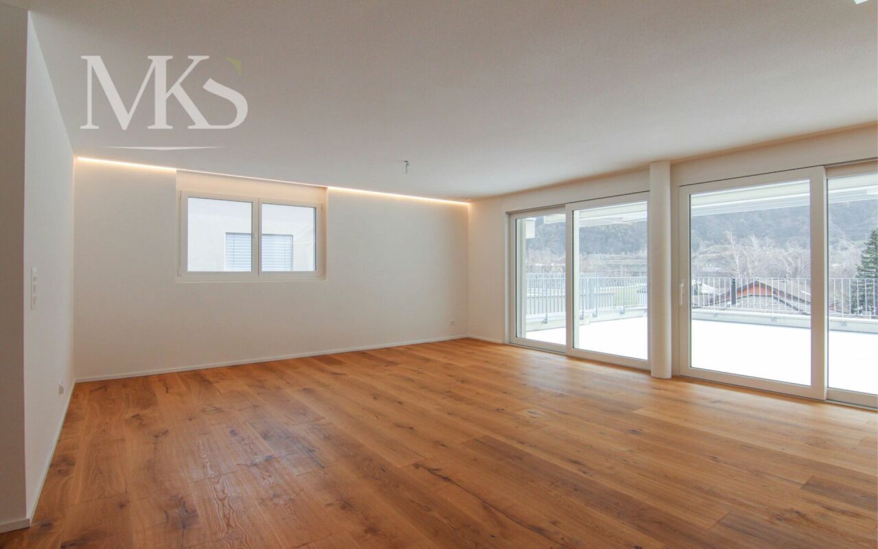 Heller, leerer Wohnraum mit Holzoptikboden und großflächigen Fenstern