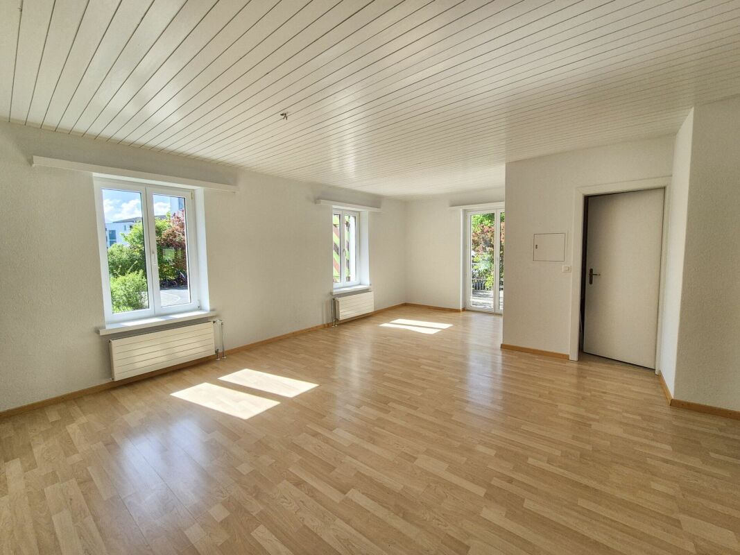 Leerer, heller Wohnraum mit Parkett und mehreren Fenstern