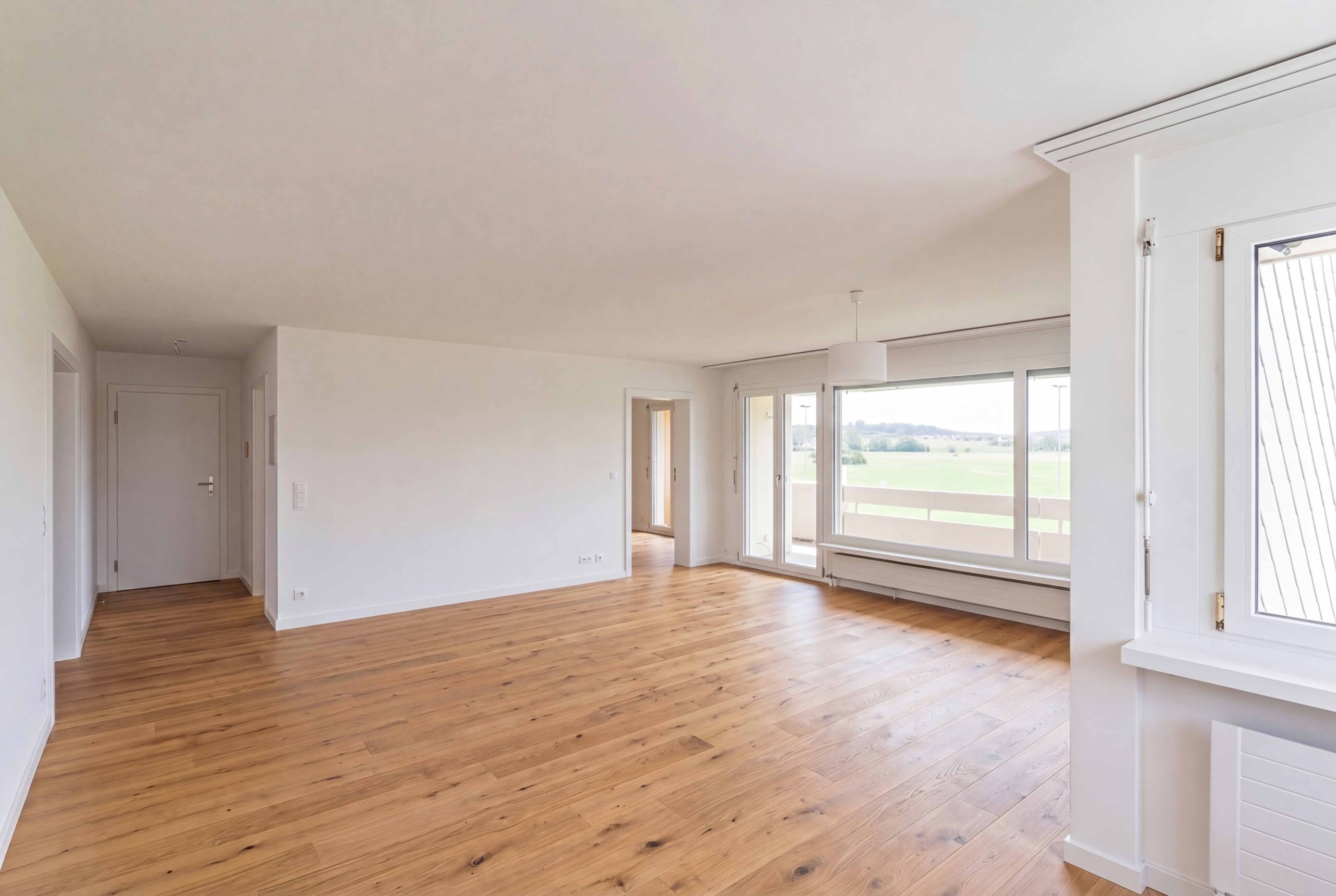 Heller leerer Wohnraum mit Holzfußboden und Panoramafenstern