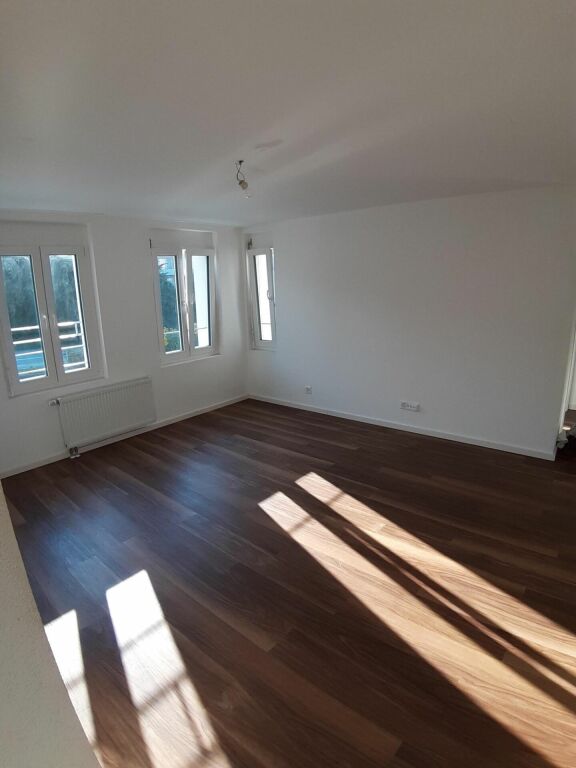 Heller leerer Wohnraum mit Holzoptik-Boden und Fenstern