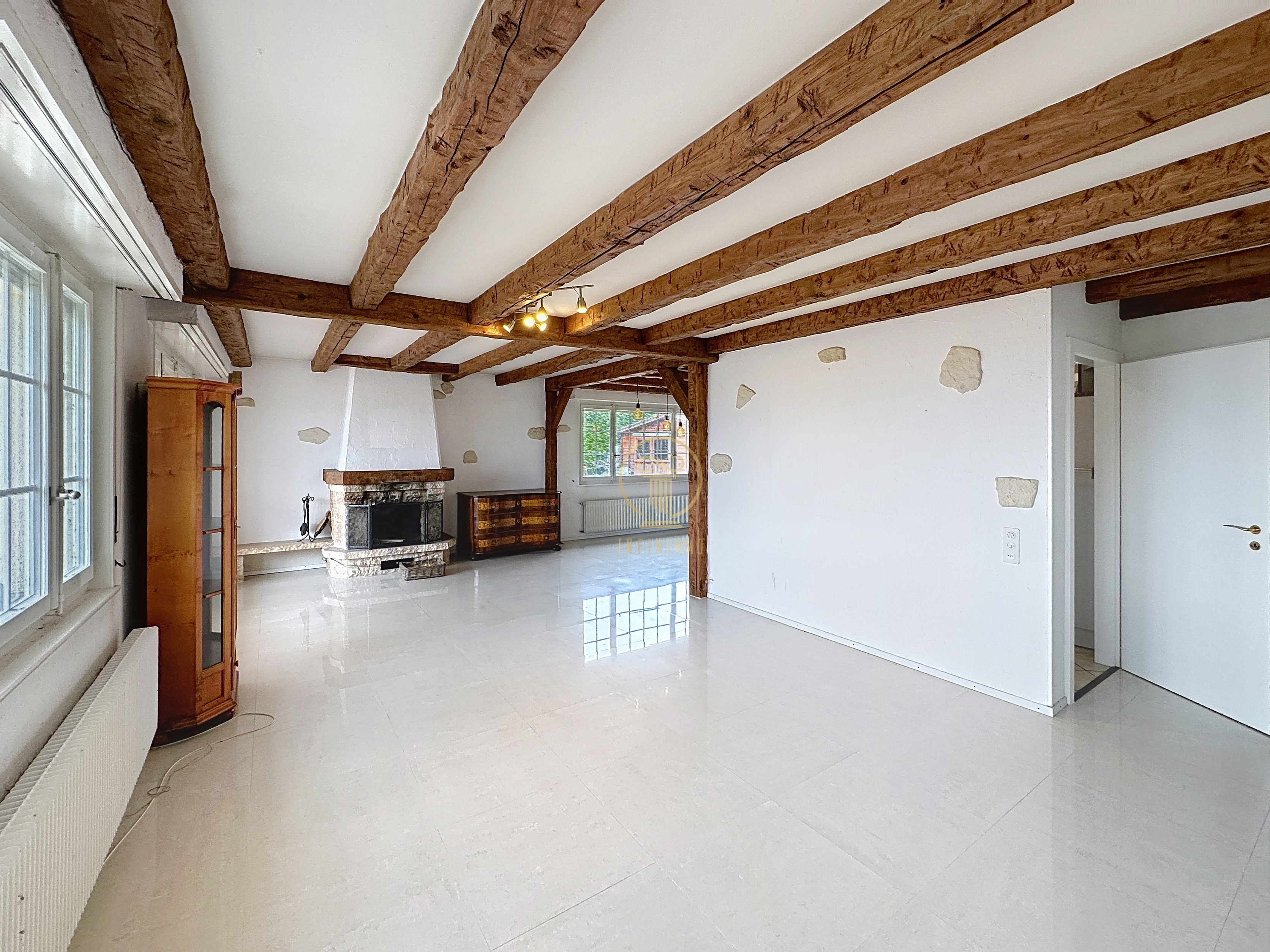 Großer Wohnraum mit sichtbaren Holzbalken und Kamin