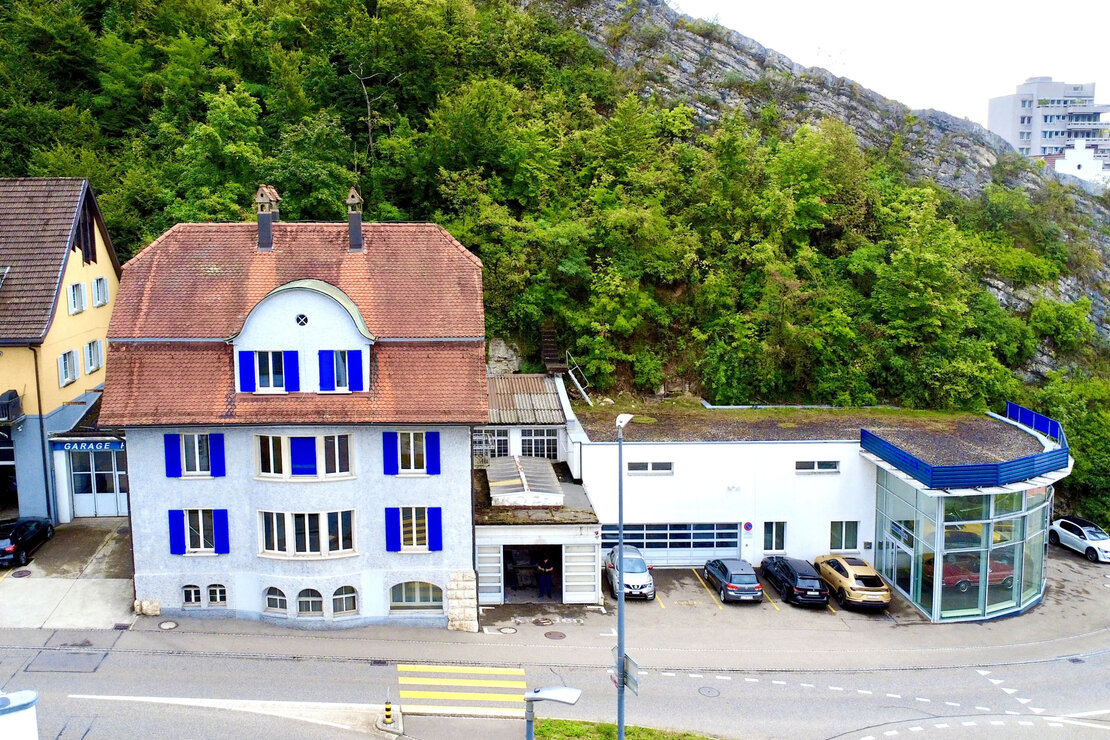 Luftaufnahme mehrerer Gebäude an einer steilen grünen Felswand