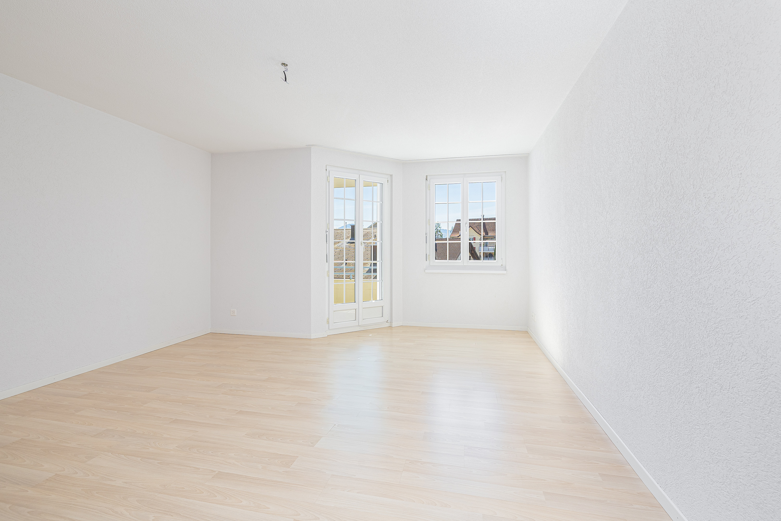 Helles, leeres Dachgeschosszimmer mit zwei Fenstern